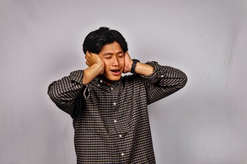 Young Man Wearing Checkered Shirt Covering Ears with Hands Expressing Discomfort in Studio