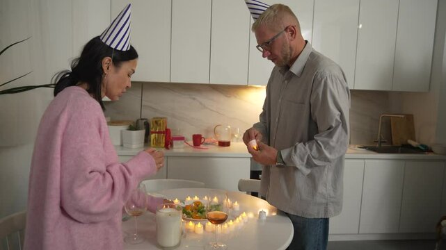 Birthday Cake Couple Kitchen - Man and woman in party hats celebrate with a birthday cake in the kitchen.