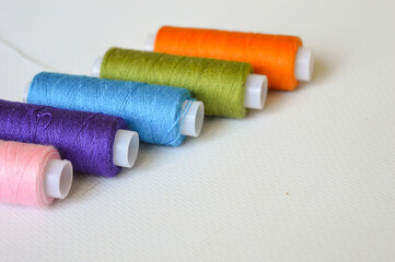 colorful spools of thread lined up on a white surface great for themes like sewing, textile arts,...