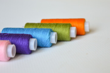 colorful spools of thread lined up on a white surface great for themes like sewing, textile arts,...