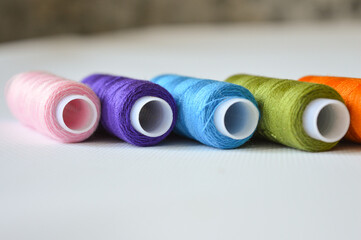 colorful spools of thread lined up on a white surface great for themes like sewing, textile arts,...