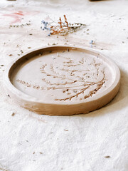 Handmade clay plate featuring delicate botanical design resting on crafting table