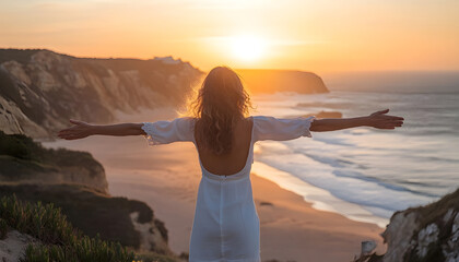 Beautiful middle aged woman standing with outstretched arms at viewpoint on picturesque Amoreira beach on Algarve coast in Portugal on sunrise