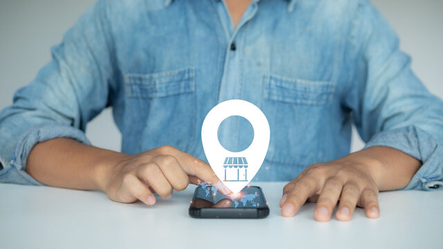 A man using a smartphone with a virtual map location icon and store symbol, representing online store location, local business search, and digital map navigation. - Powered by Adobe