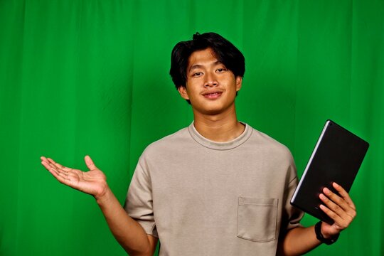 Young Man Presenting with Hand Gesture Holding Tablet in Front of Green Screen - Powered by Adobe