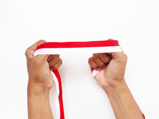The hands of a man holding a red and white ribbon as a symbol of the Indonesian flag. Isolated on white background. Independence day concept