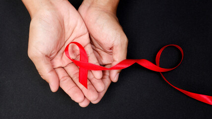 AID red ribbon in hand on a black background, a symbol of the fight against HIV, AIDS and cancer. concept of helping those in need.