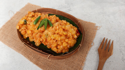 Perkedel Jagung or Bakwan Jagung, corn fritters is Indonesian traditional food. Savory snack made of corn, egg, flour, spring onion, pepper and salt. Served in wicker bamboo plate on grey background
