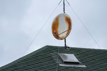 Rusty satellite dish on a rooftop under cloudy sky showcases age and wear over time in urban...