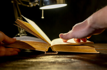 Hands gently turning the pages of an old book under warm lighting in a cozy reading space