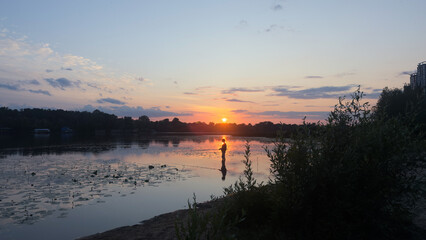 A Beautiful Sunset Over a Still Lake, Capturing the Tranquility of Nature and the Reflection of Colors in the Water under a Cloudy Sky