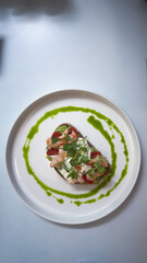 Delicious Open-Faced Sandwich with Shrimp, Fresh Greens, and Vibrant Green Sauce Perfectly Arranged on a White Plate Against a Light Background