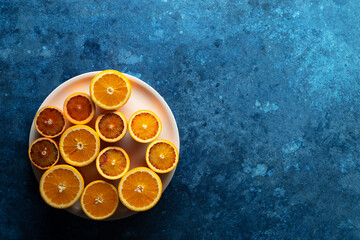 Freshly cut oranges and blood oranges arranged on a pink plate on a blue background