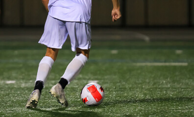 Soccer Player in White Uniform Dribbling Soccer Ball on Field at Night
