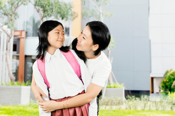 Happy Asian Mother Hugging Daughter in School Uniform Before Class Outside Modern Building