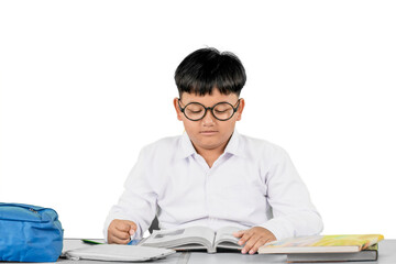 Focused Schoolboy Reading a Book at Desk with Backpack and Study Materials on White Background