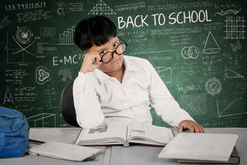 Bored Student in Classroom with Glasses Sitting at Desk in Front of Back to School Chalkboard