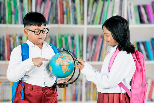 Asian school children studying a globe in the library, learning about geography