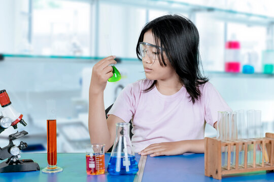 Young girl conducting chemistry experiment in school science lab with colorful liquids