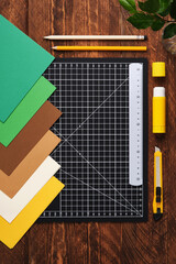 Workspace for paper crafts. Black cutting mat, colored paper, pencils, scissors, ruler, glue. Space...