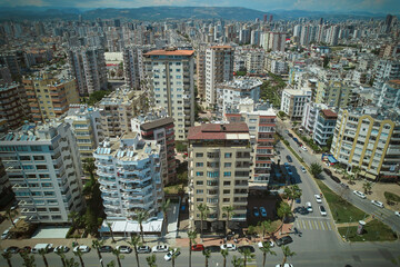 High-angle aerial view of cityscape filled with mid-rise and high-rise apartment buildings. Grid of streets, intersections and modern residential structures extending toward distant hills