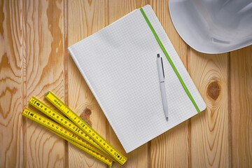 Top-down view of engineering notepad with pen, yellow folding ruler and white safety helmet on...