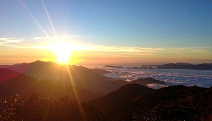 A stunning panoramic view of a golden sunrise from a mountain summit, illuminating the peaks and a sea of clouds below.