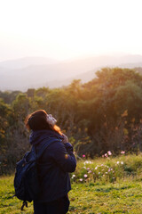 Asian young woman backpack smiling and standing with wildflower and beautiful landscape of valley Doi Luang Chiang Dao mountain, Chiang Mai Province of Thailand
