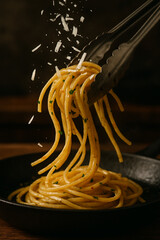 Tongs Lifting Italian Spaghetti with Falling Parmesan Cheese in Rustic Pan Setting
