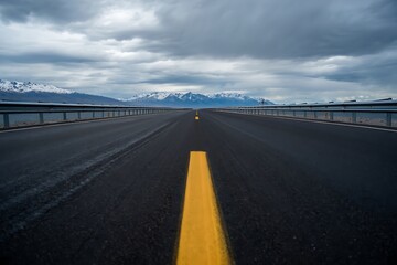Fototapeta premium A long road stretches towards snowcapped mountains under a cloudy sky