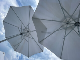 Scenic view of multiple white beach umbrellas against a cloudy blue sky, evoking a calm and...