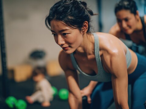 Young Asian woman doing intense weight training workout in gym with fitness partner supporting du exercise session