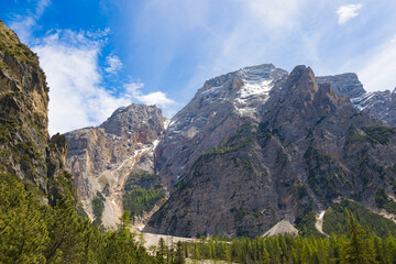 Imposing view of the Seekofel peak from Lake Braies, showcasing its rugged, rocky slopes and patches of snow amidst pine forests in the Dolomites, Italy.