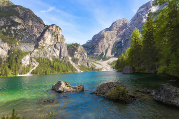 A captivating corner of Lake Braies with its crystal-clear turquoise waters, scattered rocks, and a dramatic backdrop of towering, rugged mountains and dense forests in the Dolomites, Italy.