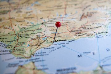 Close-up of a red-headed pin marking the city of Málaga on a world atlas map of Spain, representing travel planning, destination focus, and exploration.
