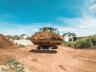 Big yellow tractor-loader is transporting earth. Preparation of construction site. Leveling the...