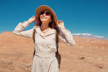 Young woman traveling through a stunning desert landscape, wearing a hat and backpack, soaking up...