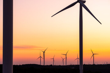 Rows of wind turbines under pink and purple skies at dawn in Catalonia symbolize renewable energy, modern sustainability goals and clean environmental progress.