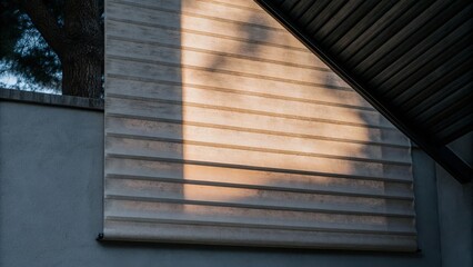 A concrete wall with horizontal lines and shadows cast by nearby trees, partially covered by a corrugated metal roof.