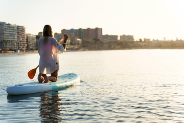 Woman kneeling on paddle board enjoying sunset over villajoyosa, spain