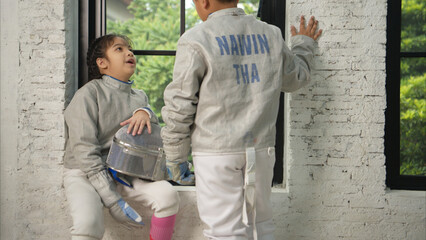 Before the tournament day, a boy and girl dressed in fencing gear are rehearsing in gym