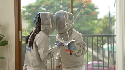 Before the tournament day, a boy and girl dressed in fencing gear are rehearsing in gym
