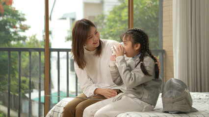 A girl in fencing gear with their mother preparing milk and sports equipment before practicing...