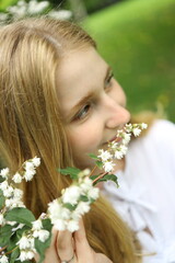 A young woman stands in a vibrant garden, gently holding a branch of delicate white flowers near...