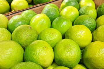 Fresh green limes in market crate. Organic citrus fruits with shiny peel. Vibrant juicy lemons for healthy lifestyle and cooking. Natural tropical food background. Freshness and vitamin C source.