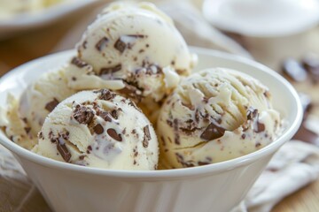 Close up of vanilla ice cream scoops topped with chocolate sprinkles, served in a stylish white bowl, creating a tempting dessert
