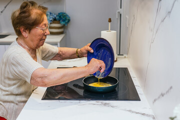 Elderly woman pouring eggs in frying pan cooking in modern kitchen