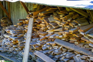 Stacks of cut wooden planks are piled under a sheltered outdoor structure.