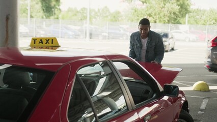 Smiling young taxi driver closing car hood on the parking.