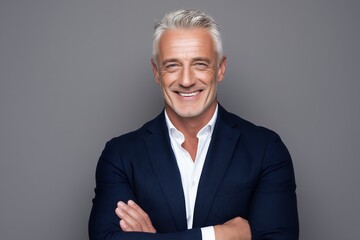 Smiling mature businessman standing with arms crossed confidently against plain grey background professional studio portrait of happy senior executive leader expressing success